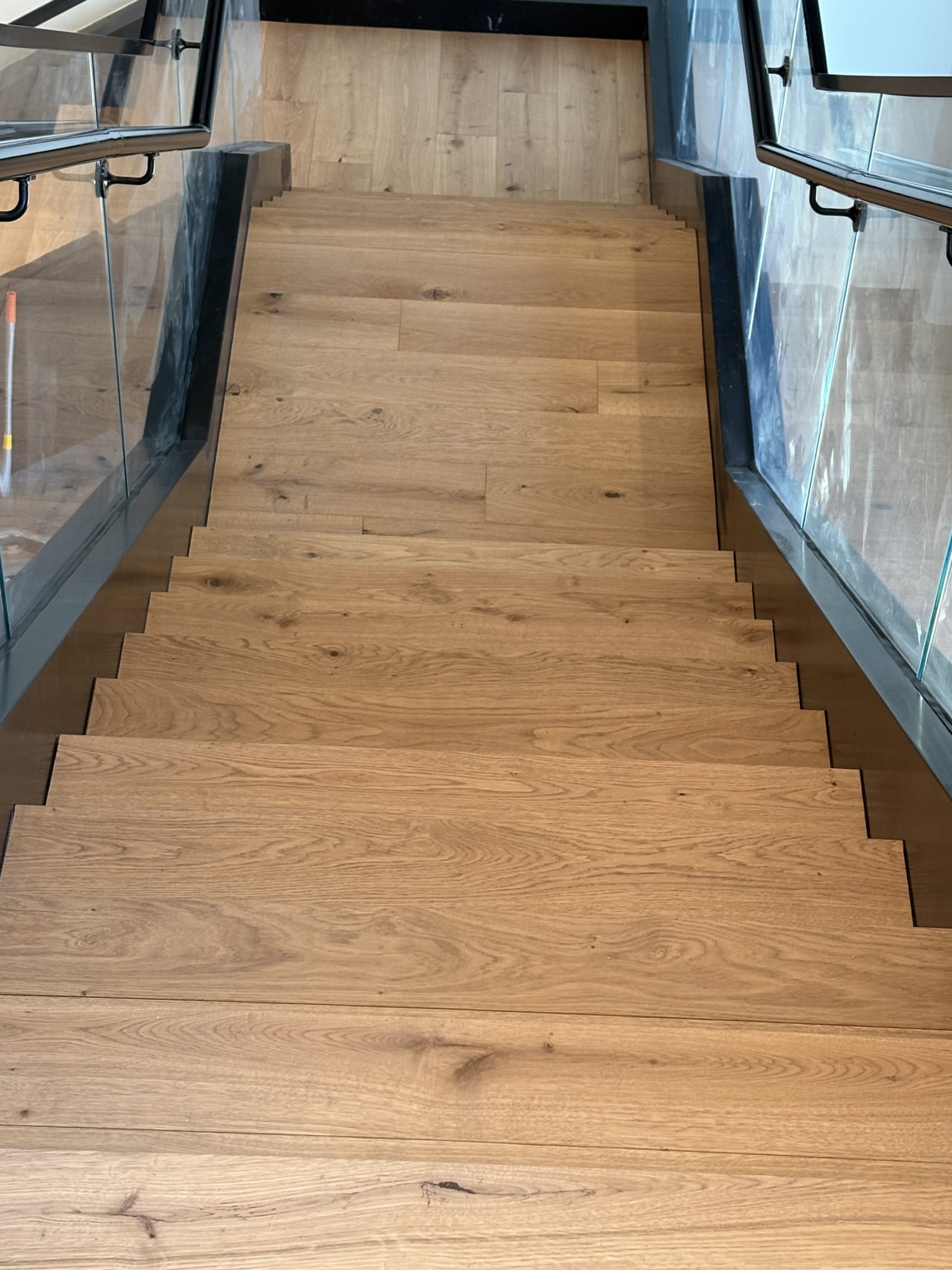 Engineered plank staircase beside a glass railing